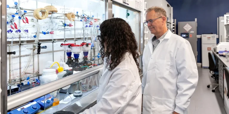 two scientists in lab coats working at a fume hood in a chemistry laboratory